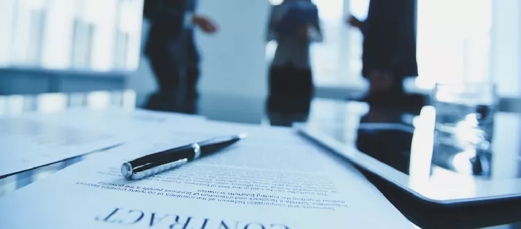 three people talking out of focus with a contract and pen on a table international business law